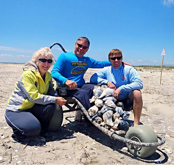Paraplegic in a Sand Rider beach wheelchair clamming on the beach with wife and son